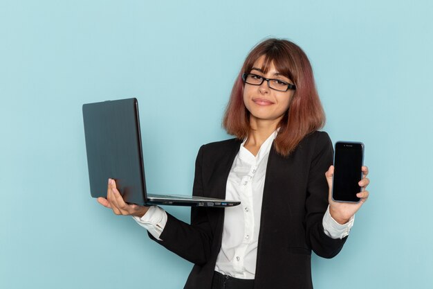 Front view female office worker holding smartphone and laptop on the blue surface