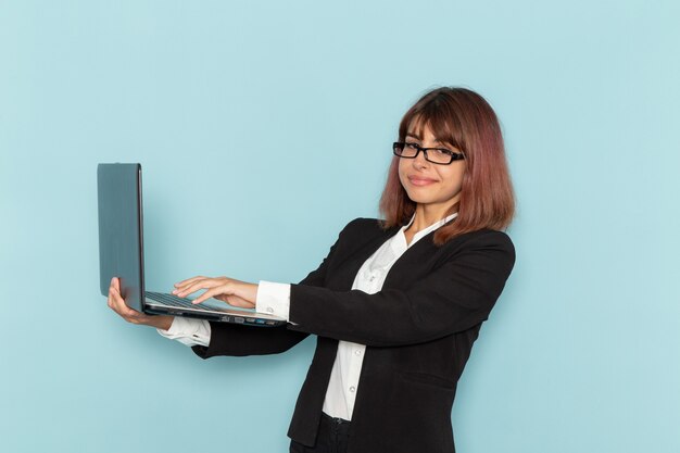 Front view female office worker in strict suit smiling and using laptop on blue surface