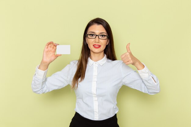 Front view of female office worker in white shirt and black skirt holding white plastic card on light-green wall