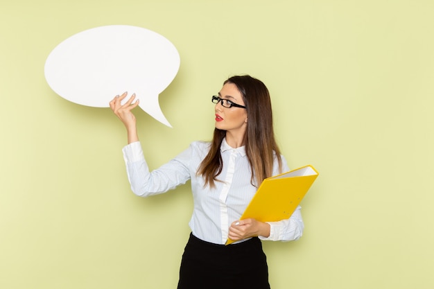 Free Photo front view of female office worker in white shirt and black skirt holding white sign and yellow file on light-green wall