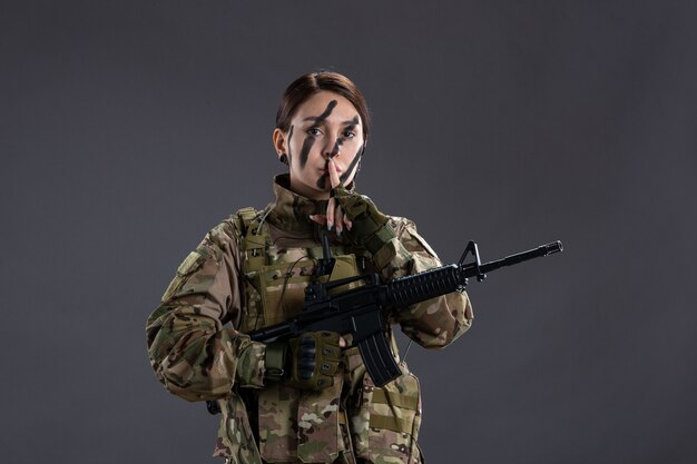 Front view female soldier in camouflage with machine gun on gray wall