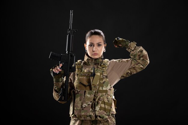 Front view female soldier in uniform with rifle on black wall