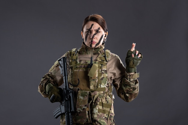 Front view female soldier with machine gun in camouflage dark wall