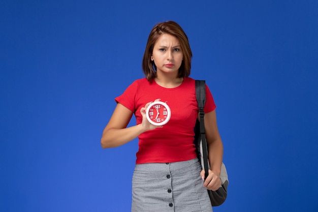 Free Photo front view of female student in red shirt with backpack holding clocks on blue wall