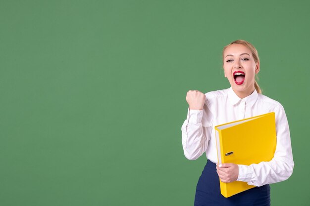 Front view female teacher posing with yellow files on green background book school woman library study university uniform work student lessons