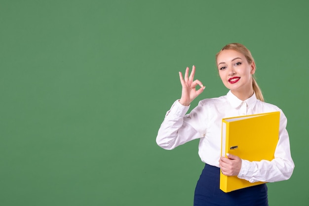 Front view female teacher posing with yellow files on green background school lesson book work student university uniform study