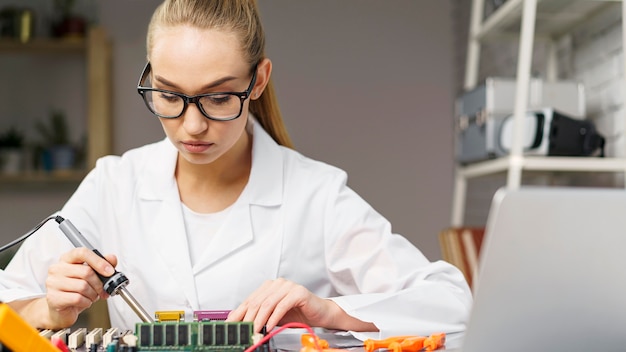 Front view of female technician with electronics board and soldering iron