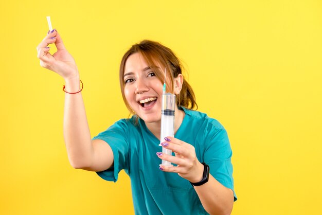 Front view of female veterinarian holding injection on yellow wall