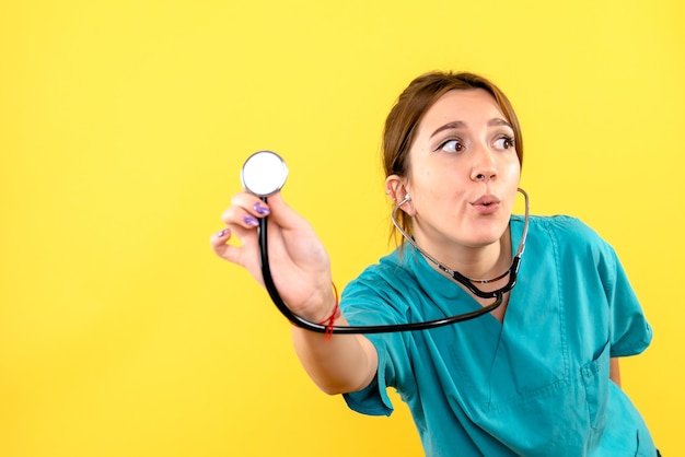 Front view of female veterinarian using stethoscope on a yellow wall