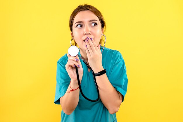 Front view of female veterinarian using stethoscope on yellow wall