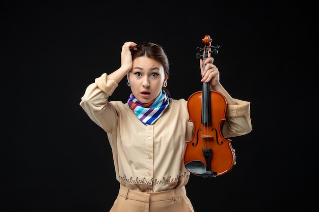 Front view female violinist holding her violin on dark wall concert melody play instrument emotion woman performance music