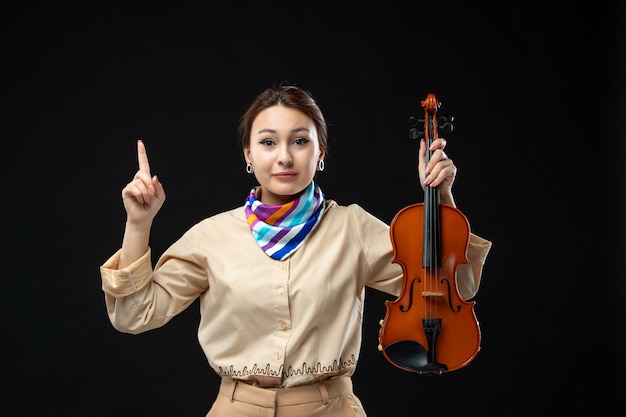 Front view female violinist holding her violin on dark wall concert melody play instrument woman performance emotion