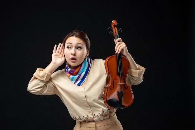 Front view female violinist holding her violin on dark wall music concert melody instrument woman performance emotion plays