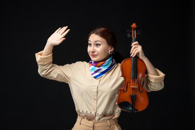 Front view female violinist holding her violin waving on dark wall concert melody instrument woman performance music emotion play