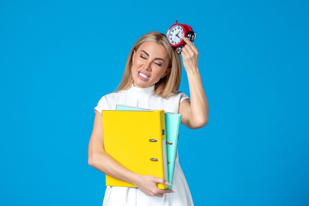 Free photo front view of female worker holding folder and clock on blue wall