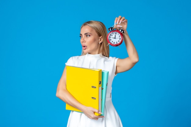 Free photo front view of female worker holding folder and clock on blue wall