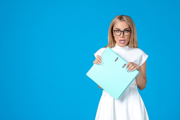 Front view of female worker in white dress holding blue folder on blue wall