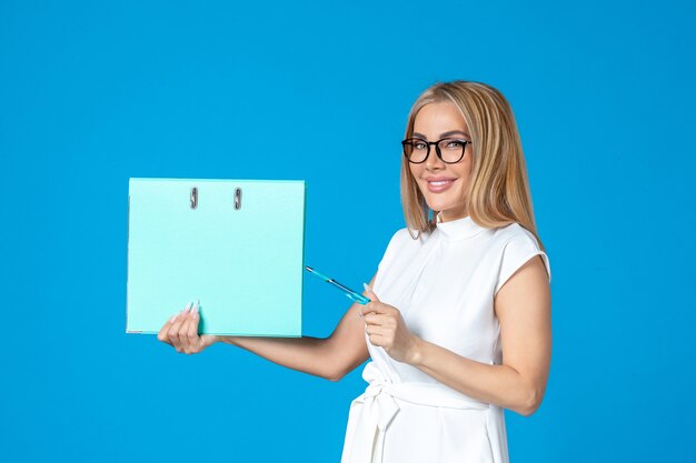 Front view of female worker in white dress holding blue folder on blue wall