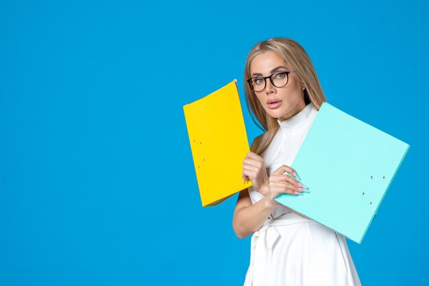 Front view of female worker in white dress holding different folder on blue wall