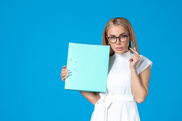 Front view of female worker in white dress holding folder on blue wall