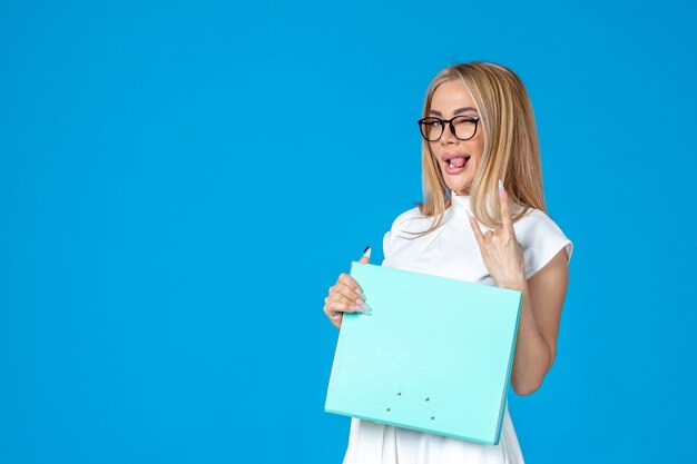 Front view of female worker in white dress holding folder on blue wall