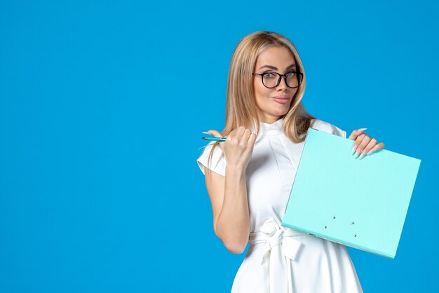 Front view of female worker in white dress holding folder on blue wall