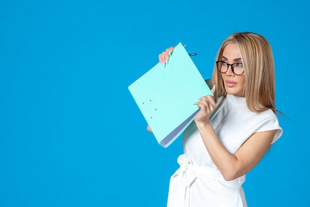 Front view of female worker in white dress holding folder on blue wall