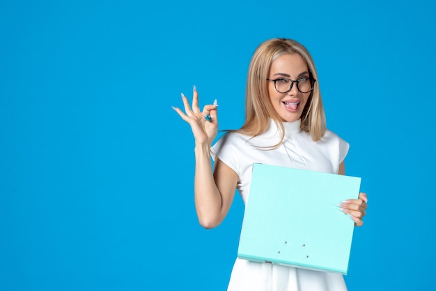 Front view of female worker in white dress holding folder on blue wall