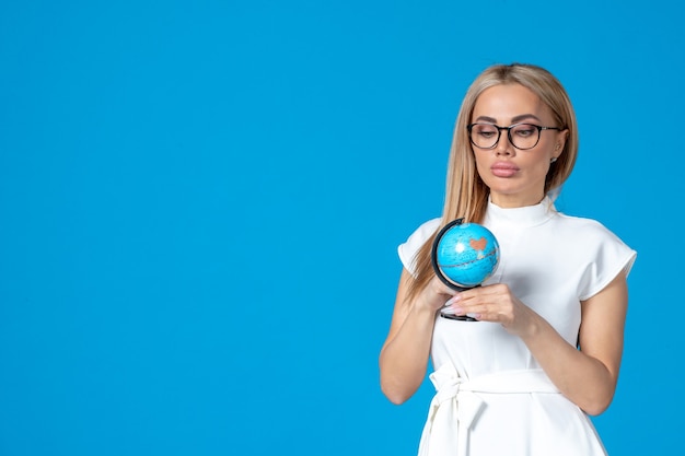 Front view of female worker in white dress holding little earth globe on blue wall