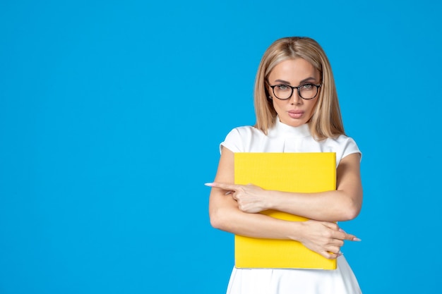 Free photo front view of female worker in white dress holding yellow folder on blue wall