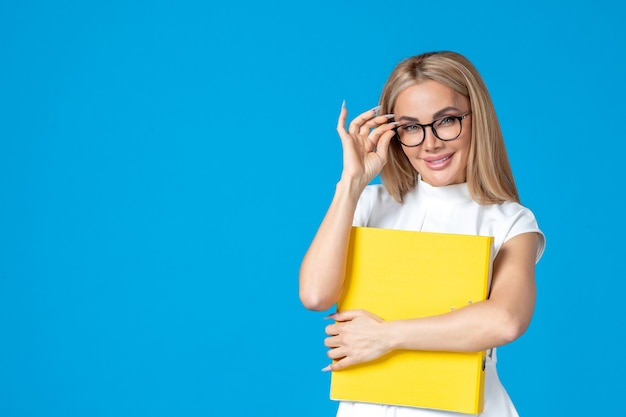 Free photo front view of female worker in white dress holding yellow folder on blue wall