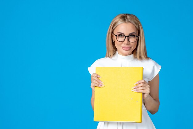 Front view of female worker in white dress holding yellow folder on blue wall