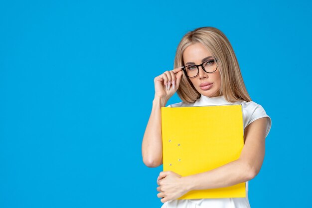 Front view of female worker in white dress holding yellow folder on blue wall