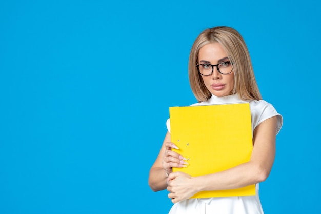 Front view of female worker in white dress holding yellow folder on blue wall