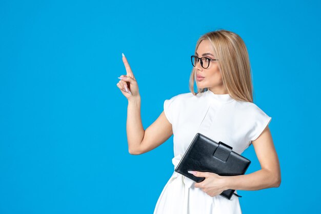 Front view of female worker in white dress posing with notepad on blue wall