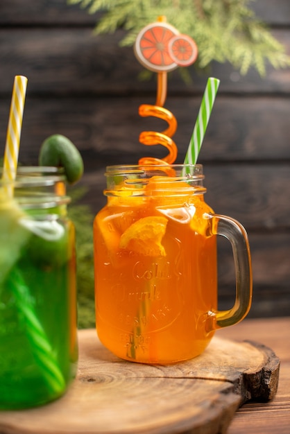 Free photo front view of fresh fruit juices in a glass served with tubes on a wooden cutting board on a brown table