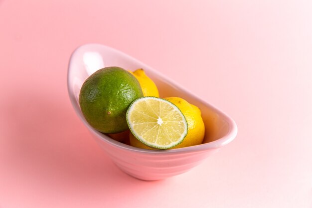 Front view of fresh lemons with sliced lime inside plate on pink wall