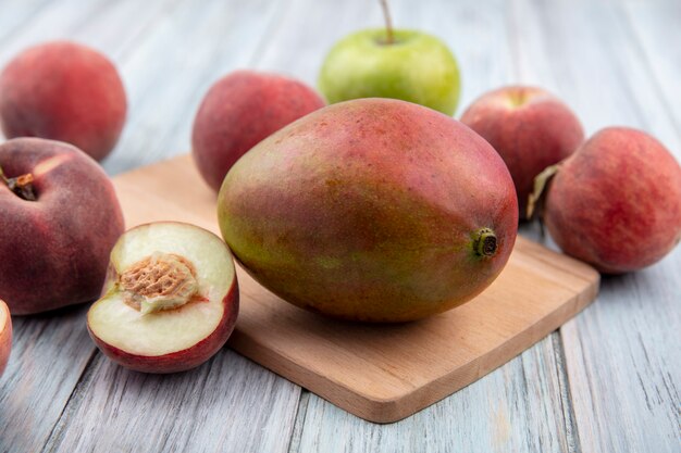 Front view of fresh mango on a wooden kitchen board with fresh fruits such as apple peach on grey wooden surface