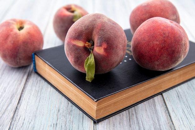 Front view of fresh peaches with leaf over a book on grey wooden surface