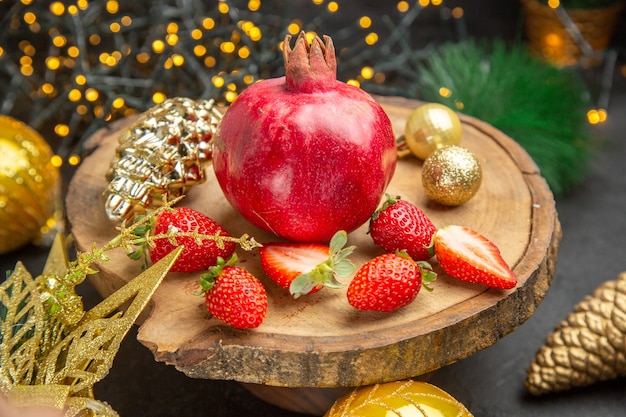 Free photo front view fresh pomegranate with strawberries around christmas toys on dark background color photo xmas holiday fruit