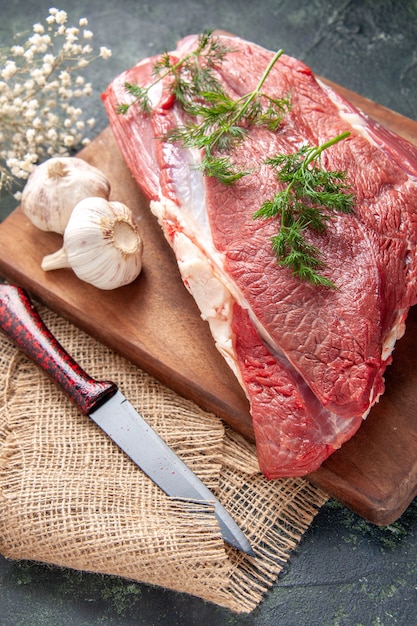 Front view of fresh raw red meats green garlics lemon salt on brown wooden cutting board knife on nude color towel on dark color background