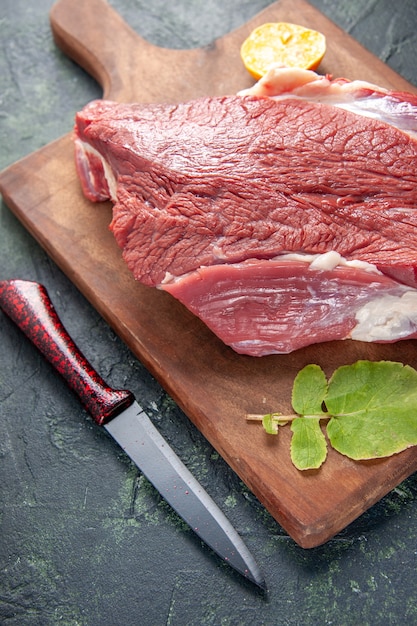 Front view of fresh raw red meats lemon on brown wooden cutting board and knife on dark color background