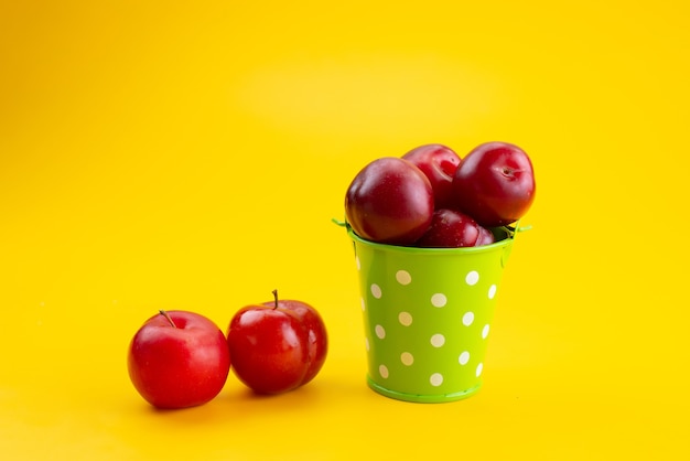 A front view fresh red plums inside green basket on yellow, fruit color sour