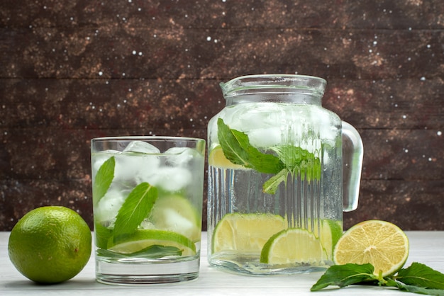 Front view fresh sour limes inside and outside glass can with lime drink on grey, fruit citrus tropical juice