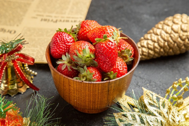 Front view fresh strawberries inside plate around christmas toys on dark background photo mellow many fruit color