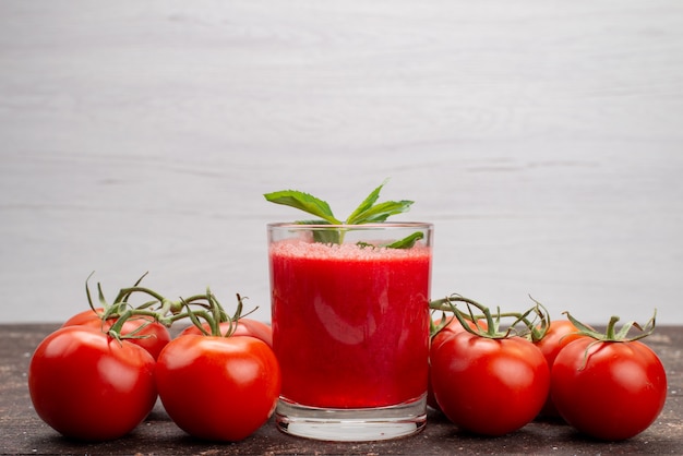 Front view fresh tomatoe juice with leaf along with whole tomatoes on grey, vegetable fruit color cocktail