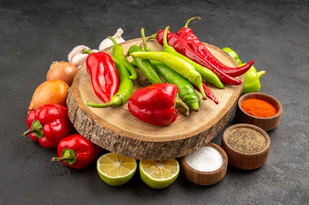 Front view fresh vegetables with seasonings and peppers on grey table