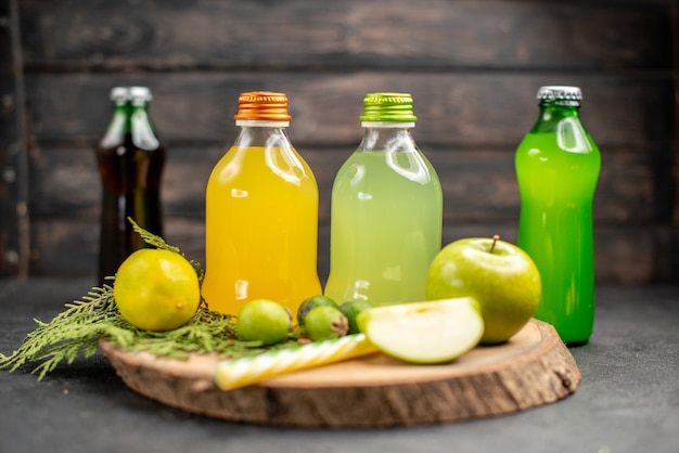 Free photo front view fruit juice in bottles apple lemon feijoas pipettes on wood board lemonades on dark surface