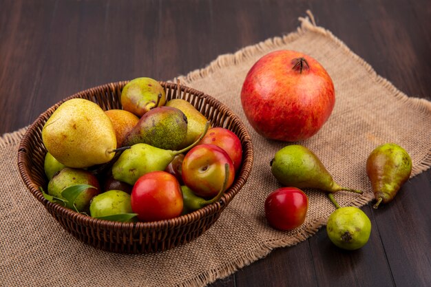 Front view of fruits as peach apple plum in basket with pomegranate on sackcloth on wooden surface