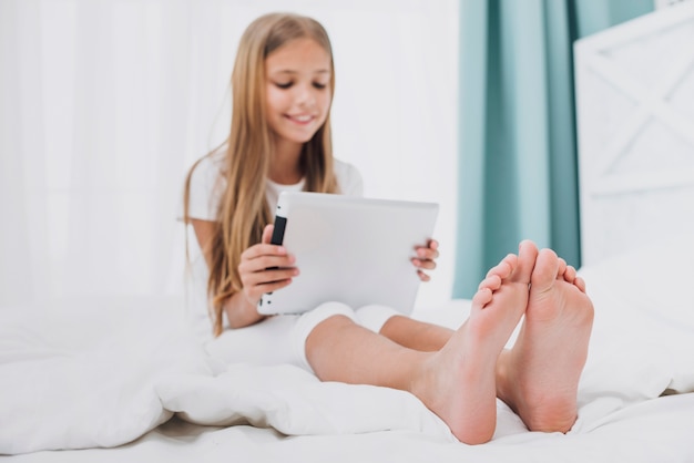 Front view girl playing on tablet in bed